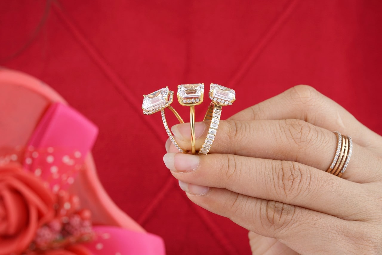 A woman holds three gold emerald cut diamond rings, each a different style.