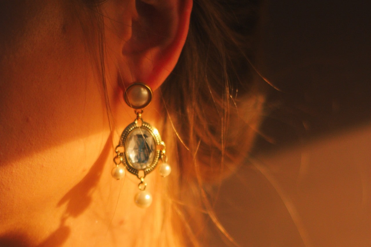 A close-up of an intricate pearl and quartz drop earring worn with the woman’s hair swept bank it’s a clip