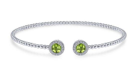A silver cuff bracelet with two round cut peridot gems and diamond halos