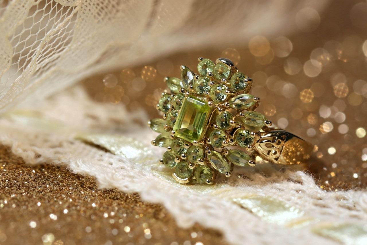 An elaborately designed peridot ring on a glittery surface
