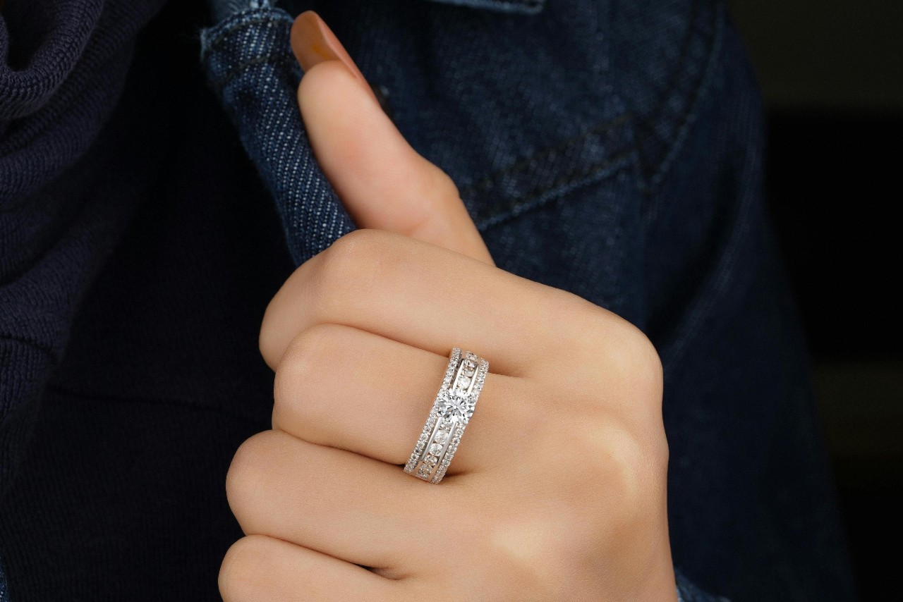 A close-up of a woman’s manicured hand against a dark denim jacket, an elegant and ornate platinum band on her finger.
