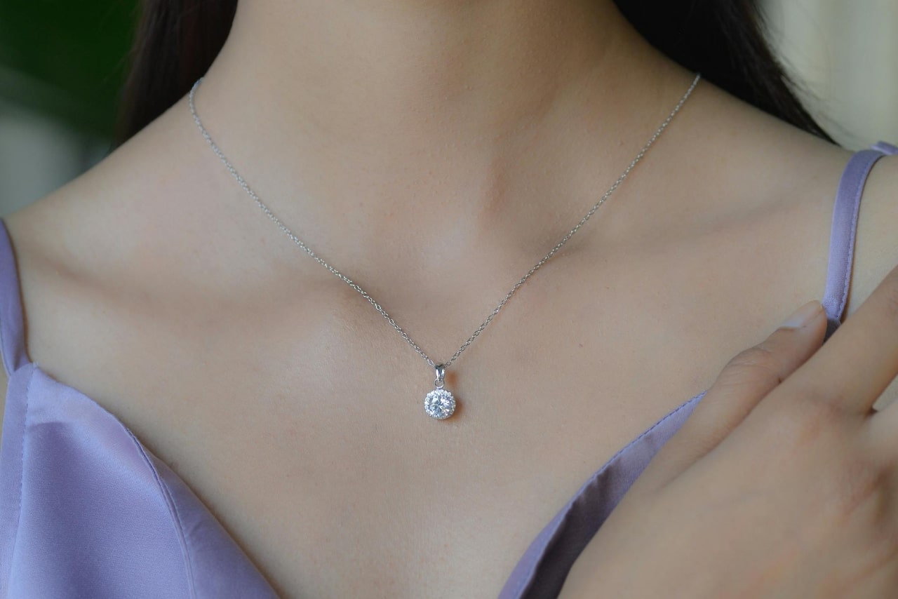 A close-up of the decolletage of a woman in a formal dress, adorned with a delicate platinum diamond pendant necklace.