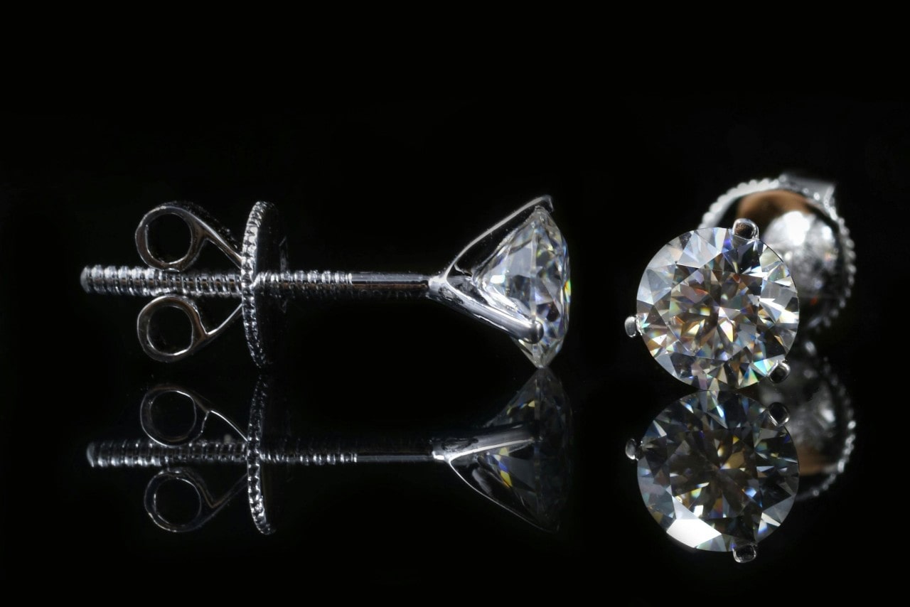 A close-up of a dazzling pair of platinum diamond stud earrings on a black backdrop.