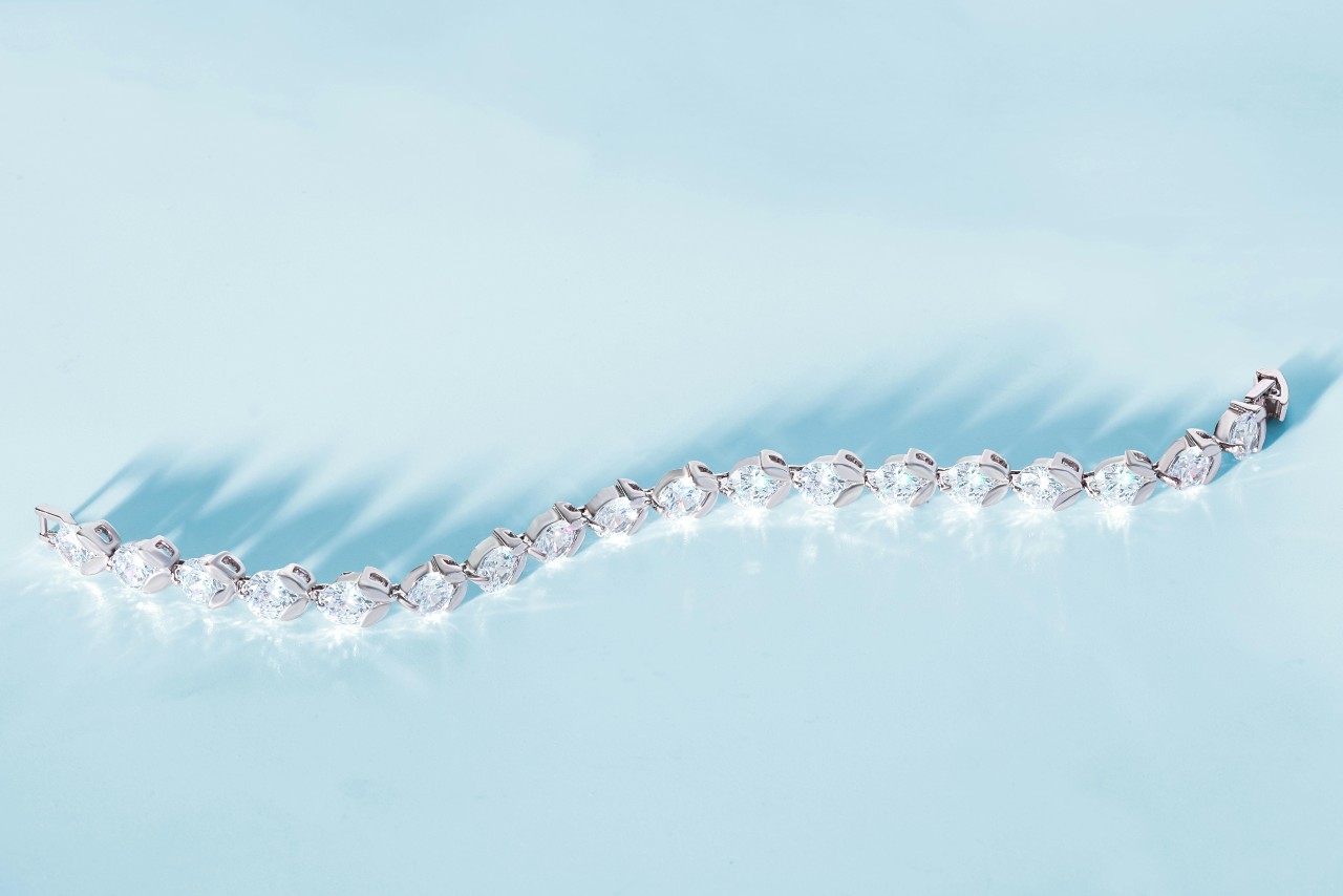 A close-up of a luminous platinum and diamond tennis bracelet on a sky blue backdrop.