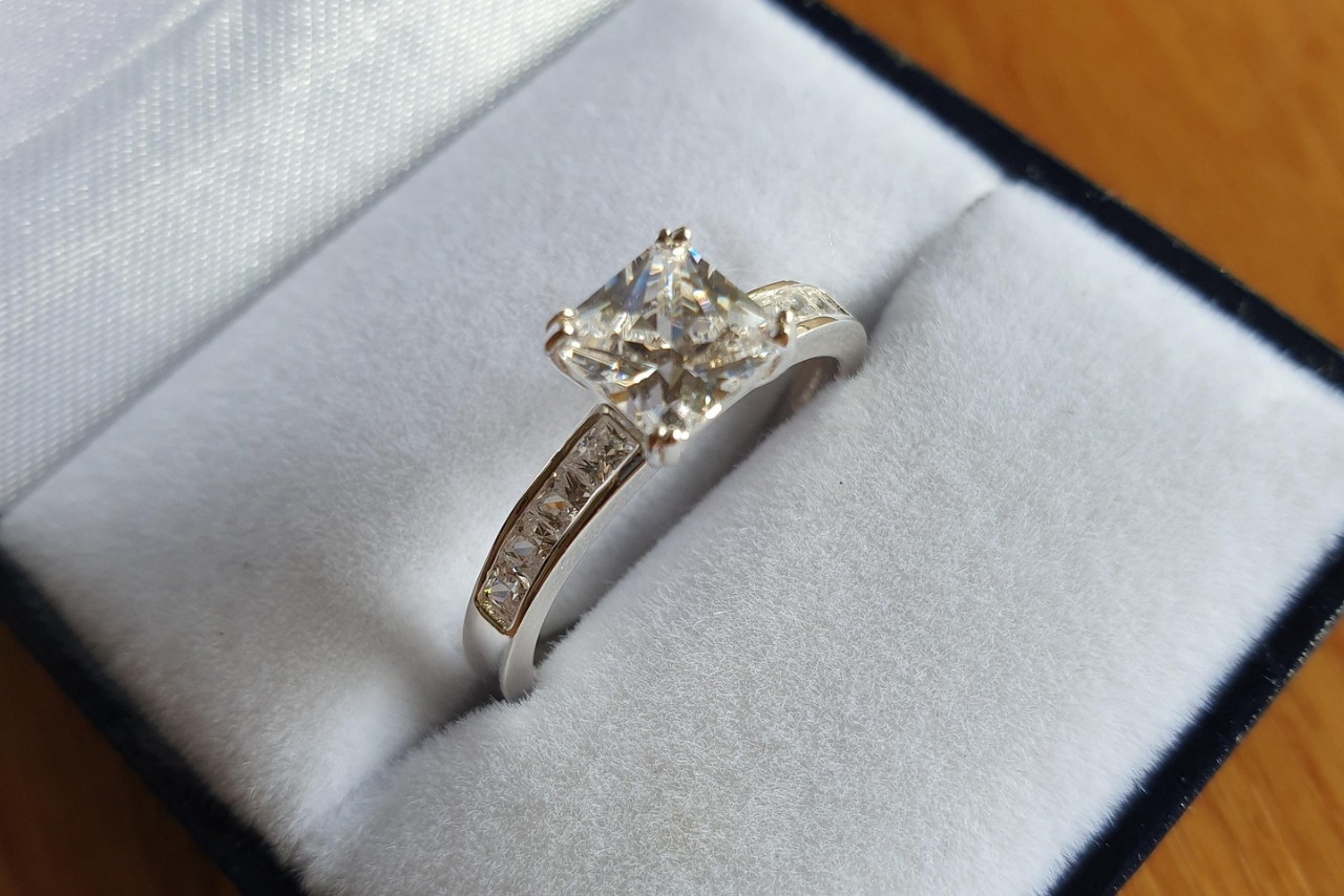 A close-up of a princess cut side stone engagement ring in a white and blue velvet ring box.