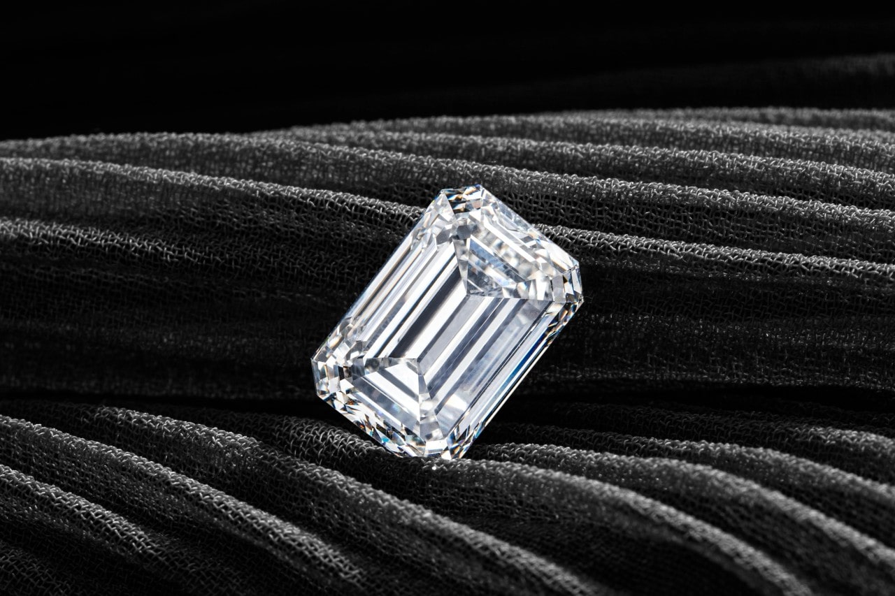 An spectacular emerald-cut diamond on black textured fabric.