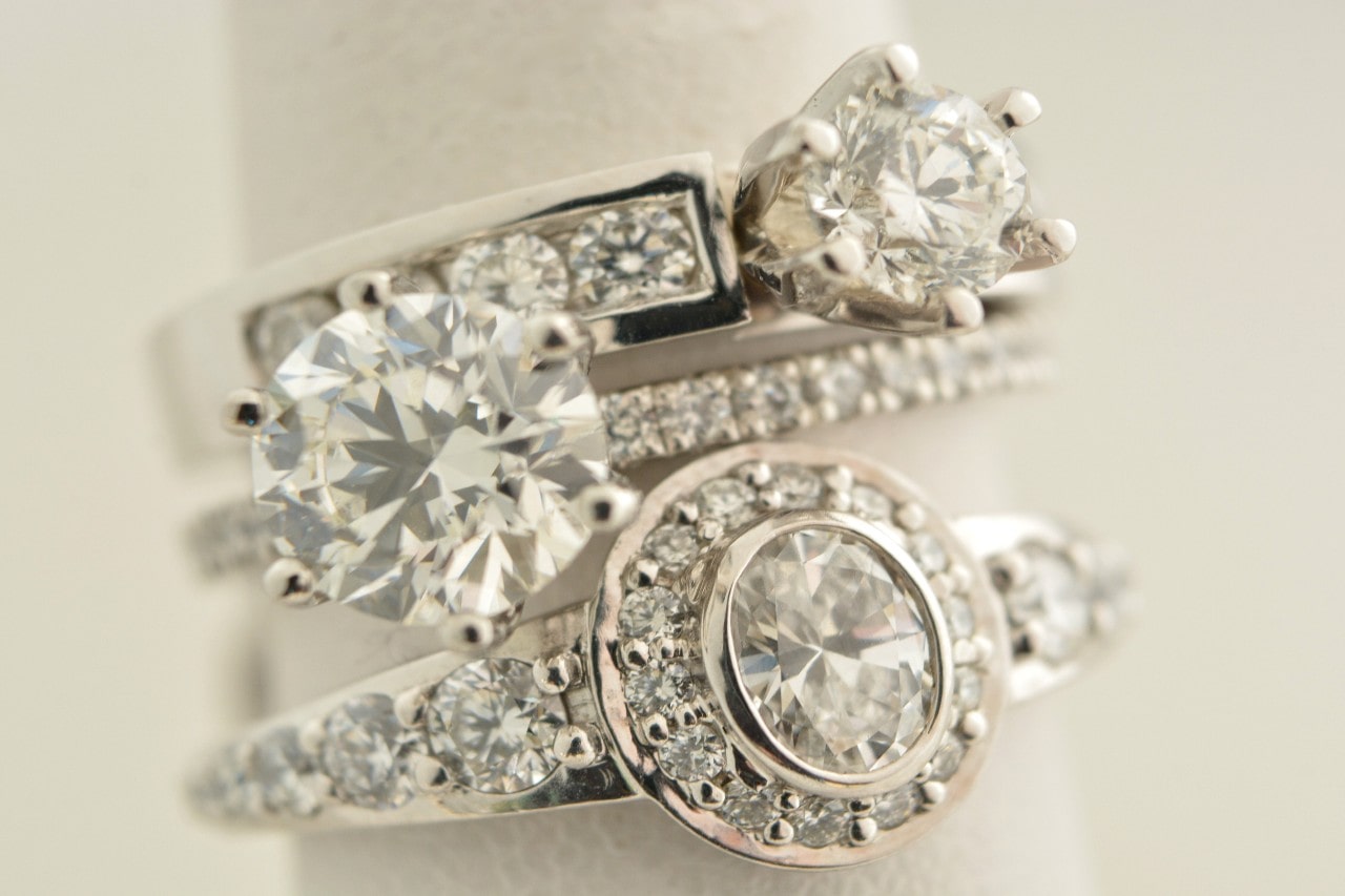 A close-up of three stacked, elegant diamond rings with multiple cuts and settings on a soft eggshell-color background.
