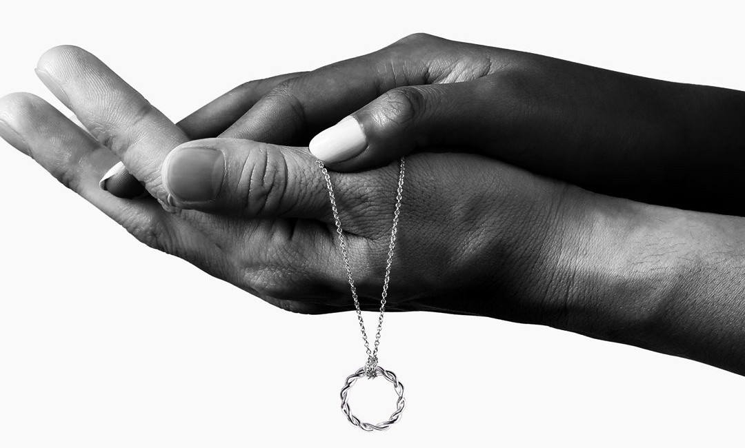 A man and woman’s hand together holding a circle necklace by Gabriel & Co.