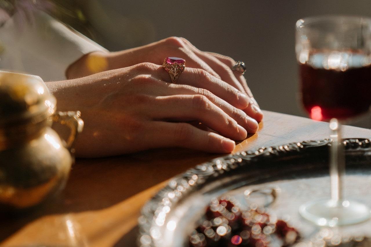 a pair of hands resting on an elaborately set table and adorned with two gemstone rings