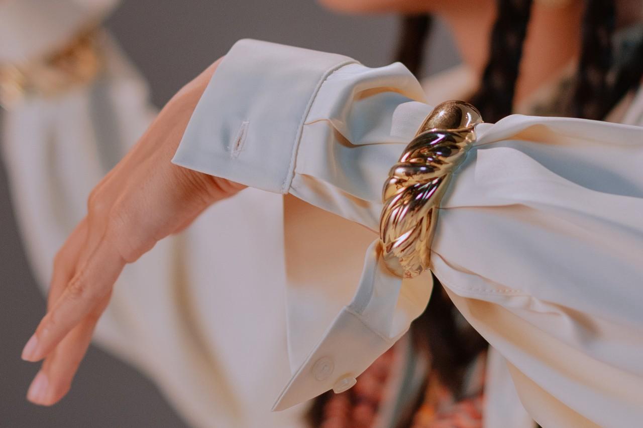 a woman’s wrist adorned in a white shirt sleeve and a chunky gold bracelet