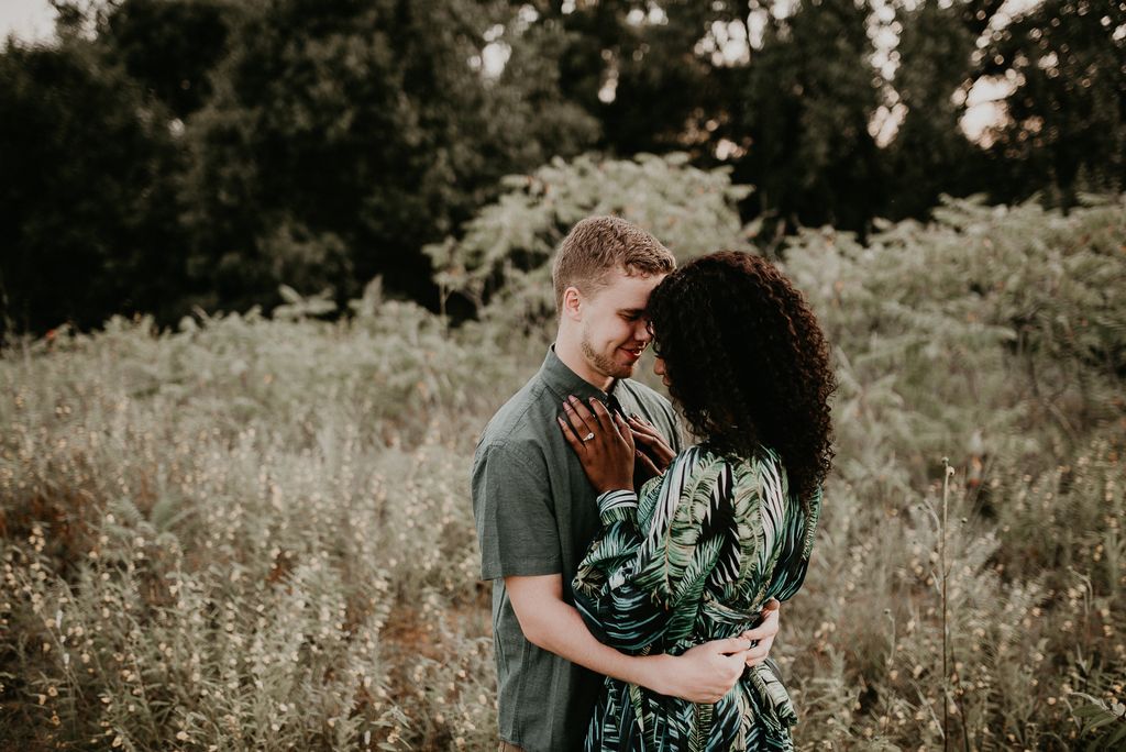 A couple embracing each other against a hill full of grass.