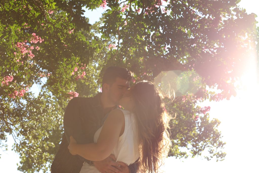 A couple kissing against a sunlight background with trees
