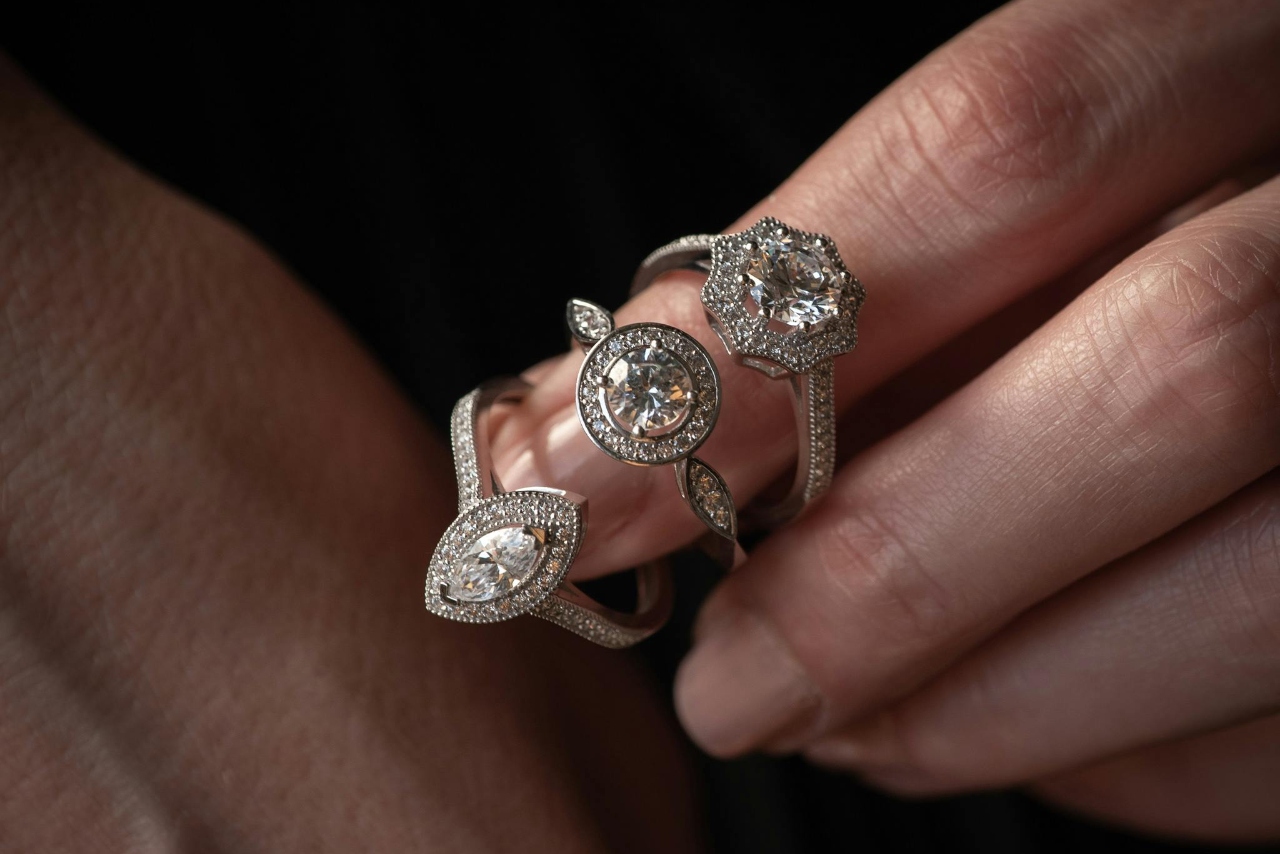 Three engagement rings with different diamond shapes looped around a manicured finger.
