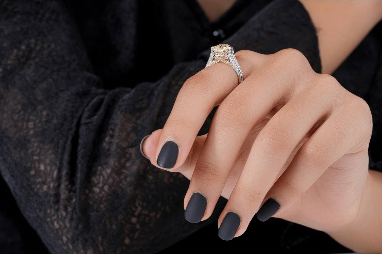 A close-up of a hand with dark black nail polish, wearing a diamond engagement ring.