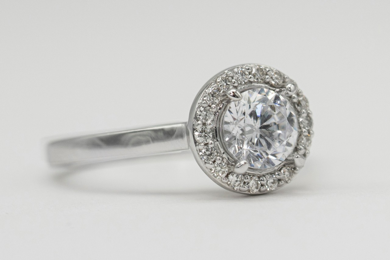 A close up of a round halo diamond engagement ring set in white gold against a white background.