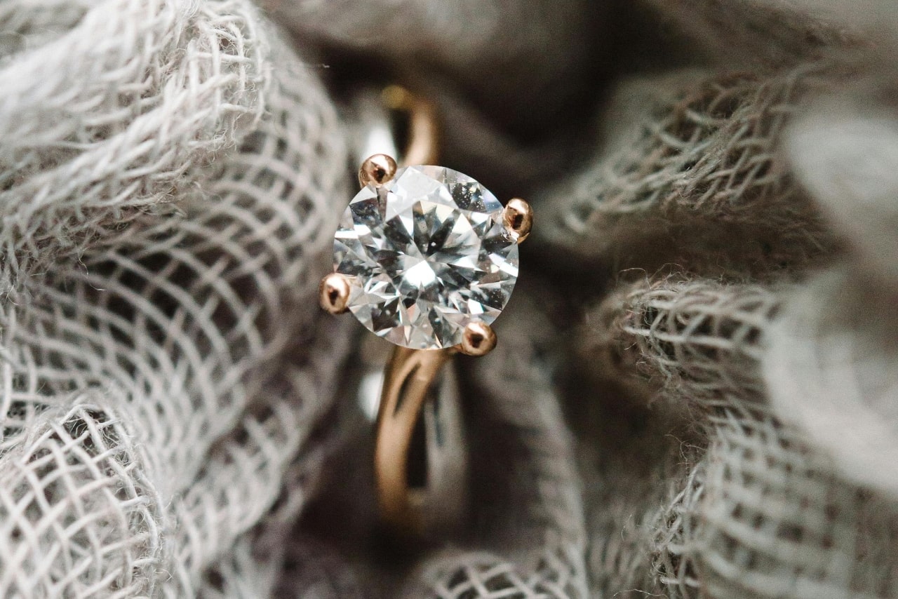 A yellow gold solitaire round cut engagement ring surrounded by grey fabric