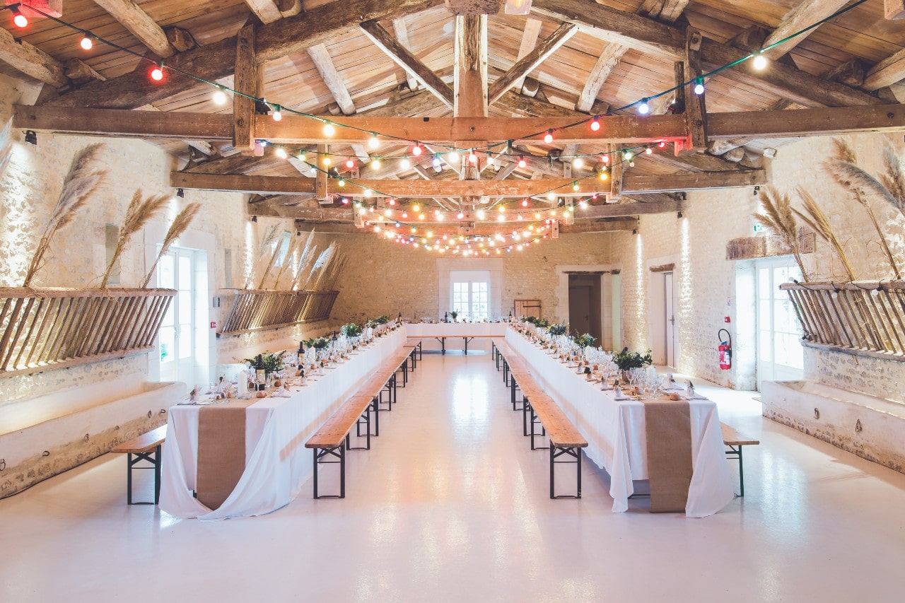 A beautifully set table for a wedding, set inside a warmly lit barn-style building.