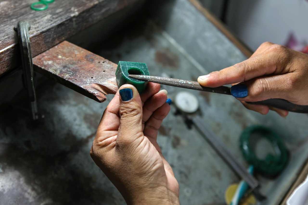 Hands carefully file a green wax ring model at a jeweler&rsquo;s bench, shaping the design before it is cast into metal.