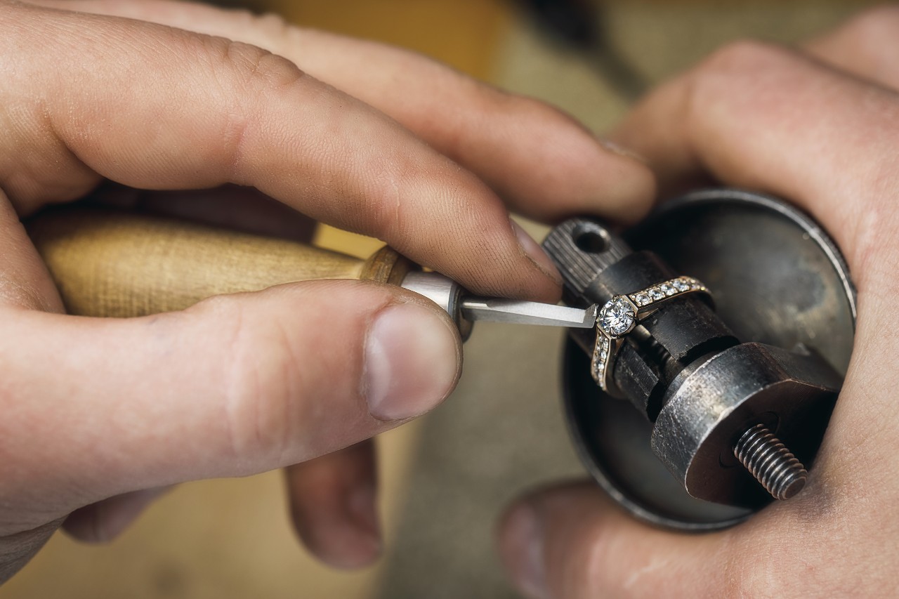 A close up of a jeweler fixing a side stone engagement ring with specific tools.