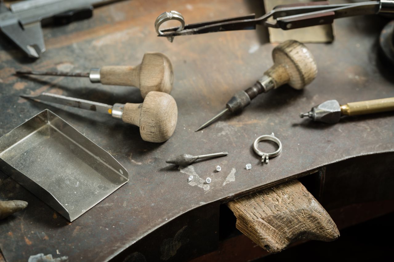 Jewelry-making tools, loose diamonds, and a partially finished ring are arranged on a worn workbench, illustrating the craftsmanship behind fine jewelry creation.
