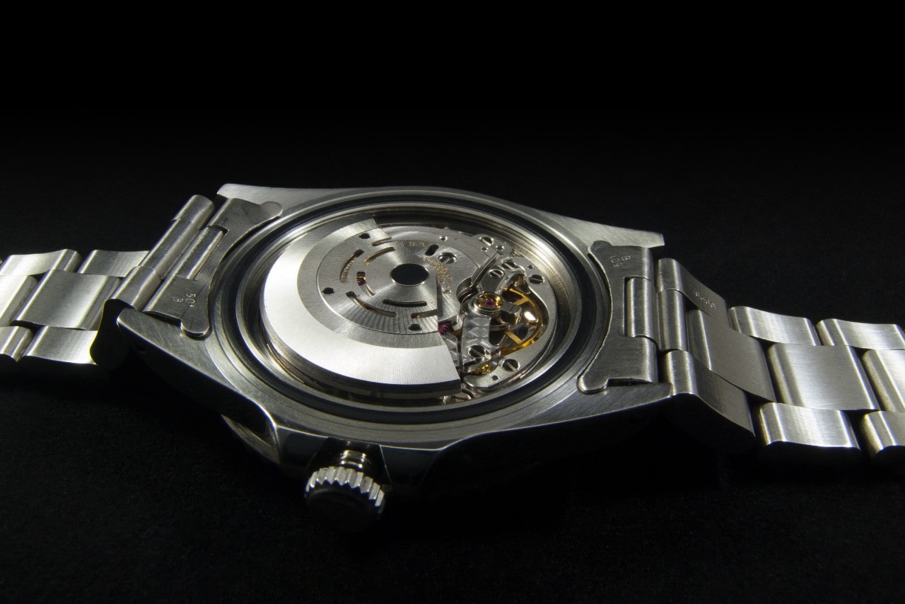 The posterior view of a watch, revealing inside workings, on a black surface.