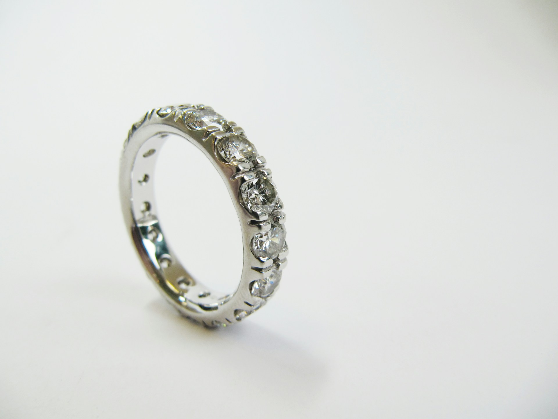 A white gold eternity band with a series of sparkling diamonds encircling it rests on a white surface.