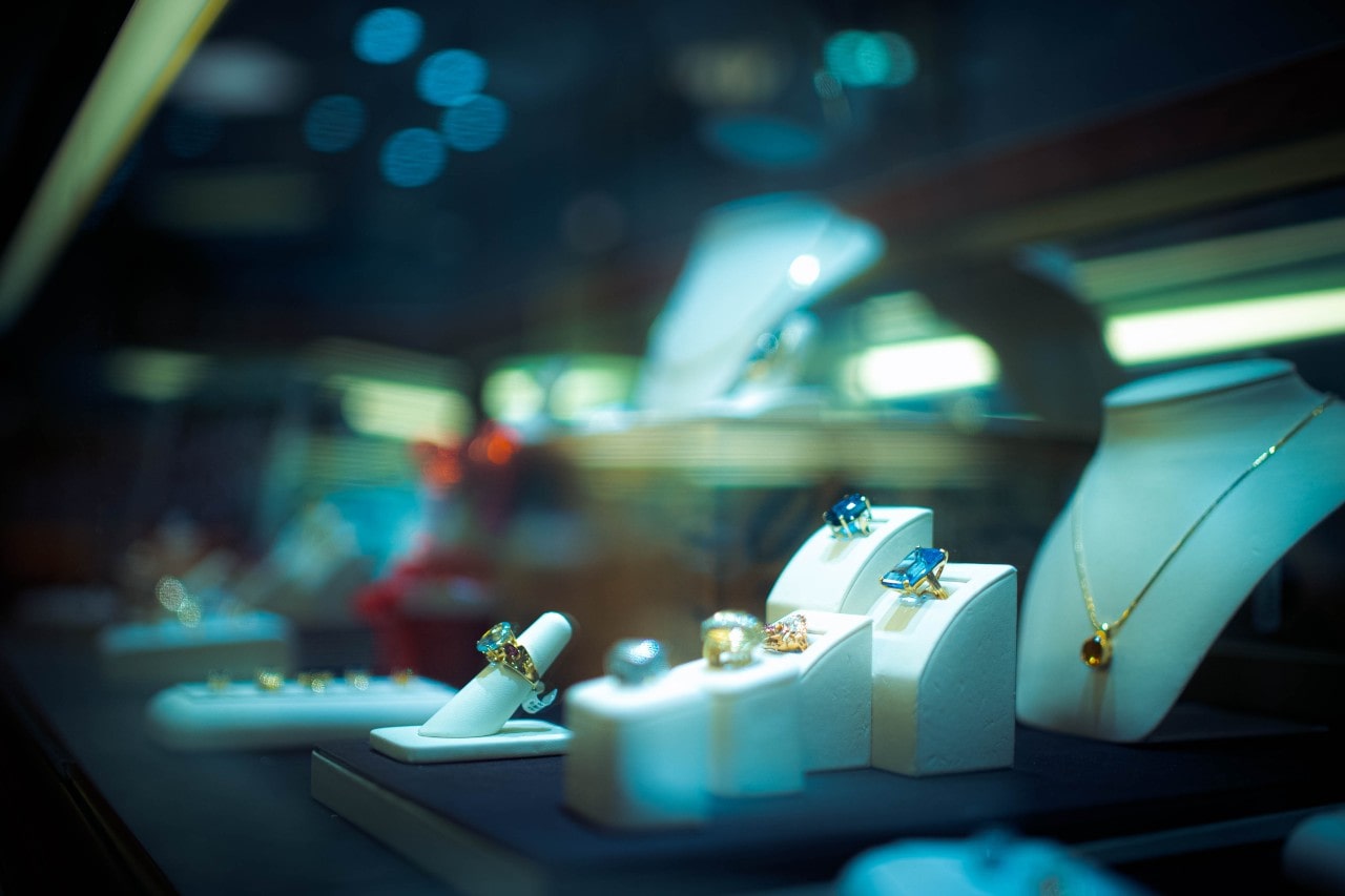 A view of a jewelry store display under night lighting featuring colorful gemstone necklaces and rings