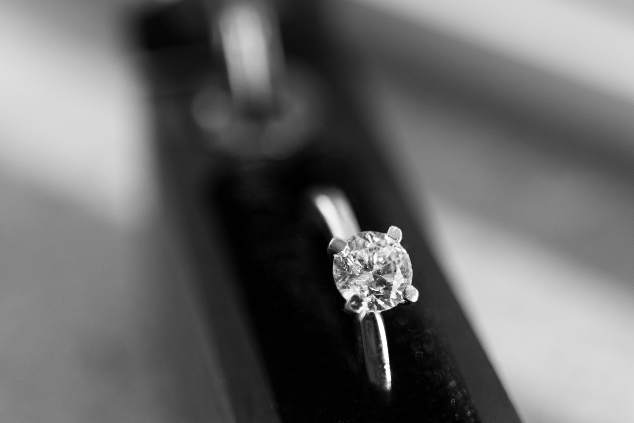 A black and white close-up of a jewelry store engagement ring display, with focus on a simple solitaire ring held upright at the front.