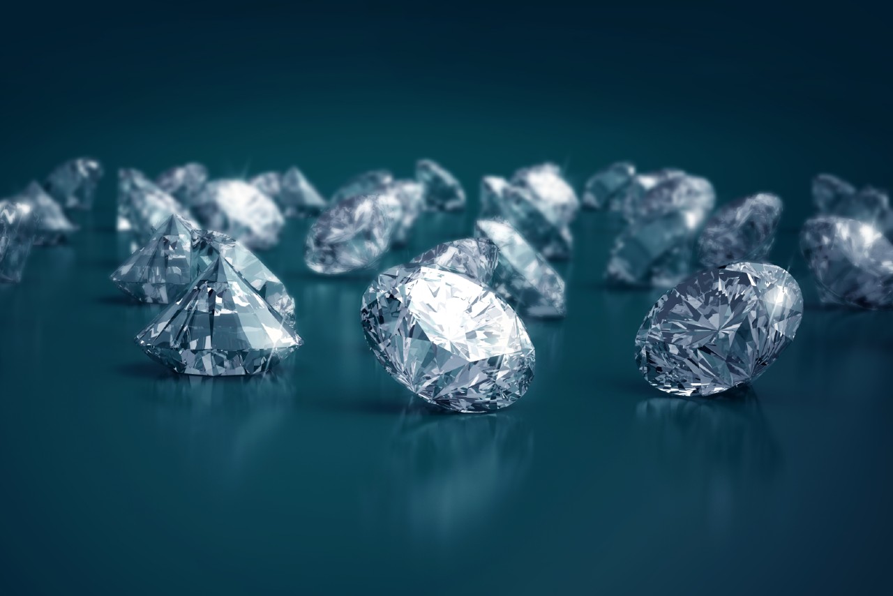 A closeup of a myriad of expertly cut diamonds sitting on a dark teal background