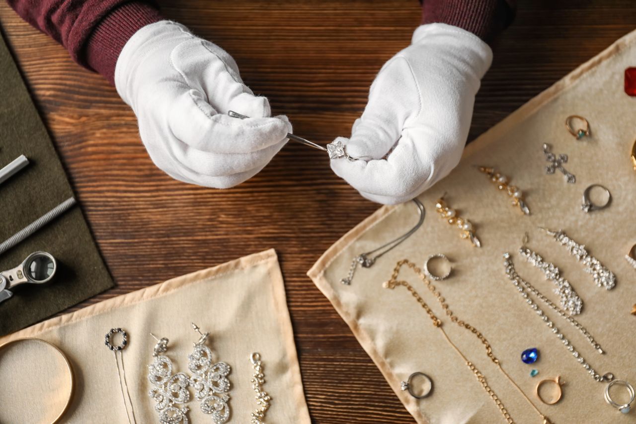An jewelry collector carefully inspects a princess-cut diamond ring while the rest of their jewelry is laid out to dry after a routine cleaning