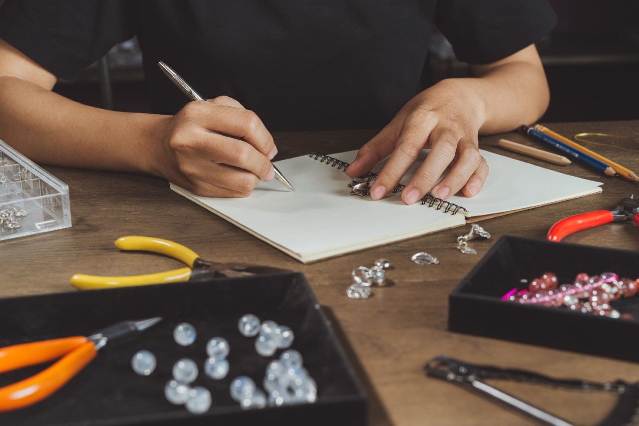 A jewelry designer sketches a design he has in mind while holding an inspiration piece