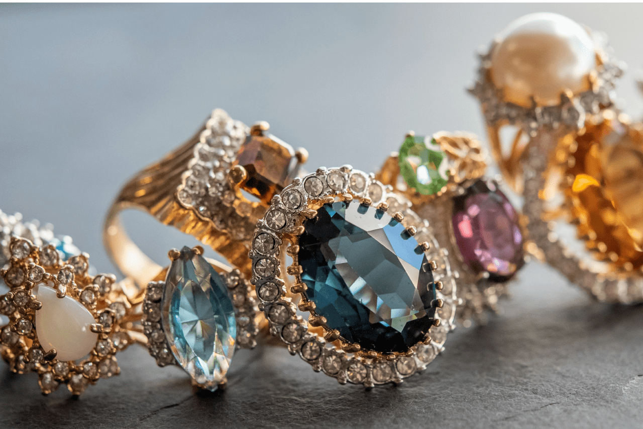 An assortment of vintage-style gemstone rings sit on a faux gray leather background