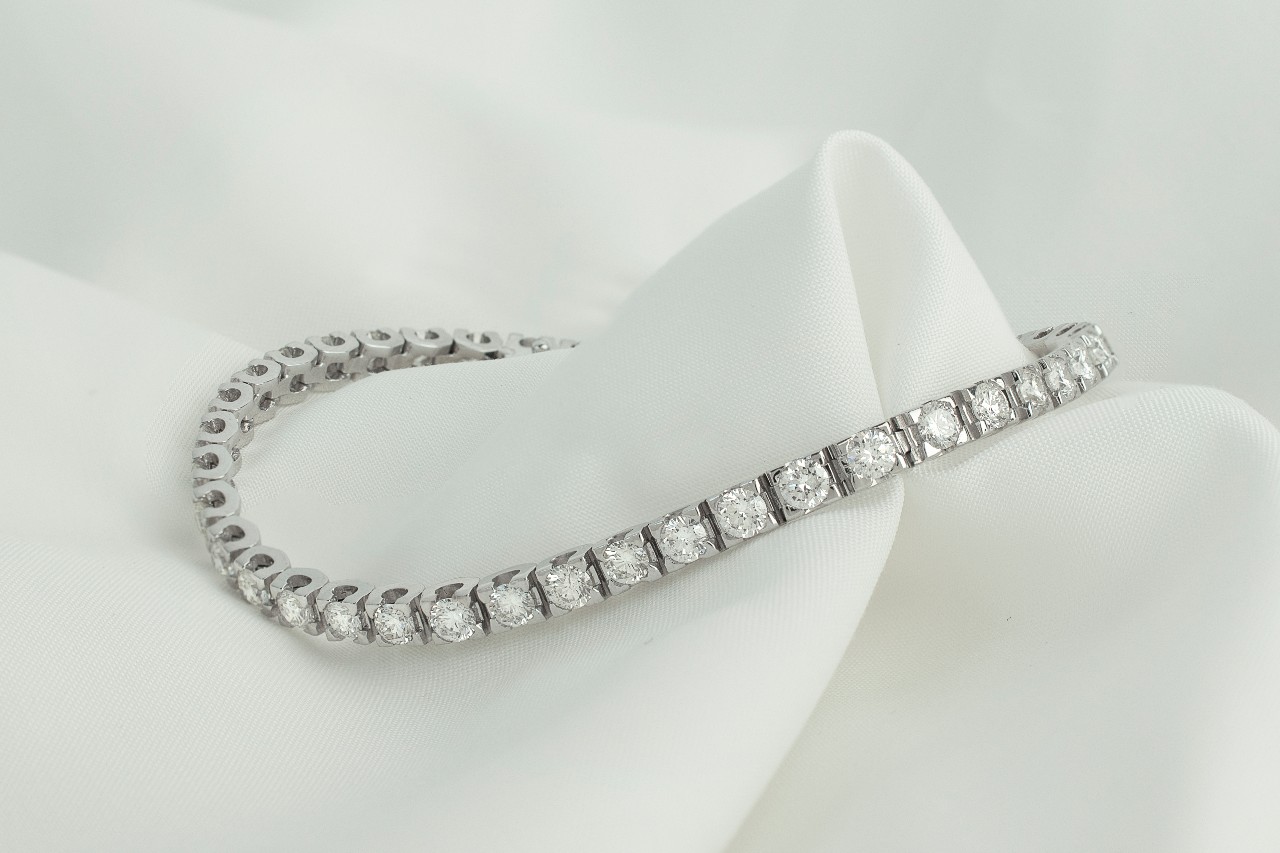 Elegant diamond tennis bracelet with a series of sparkling gems, delicately draped over smooth white fabric.