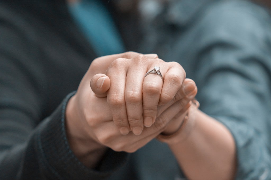 A couple holding hands, highlighting a classic solitaire engagement ring on the woman's finger