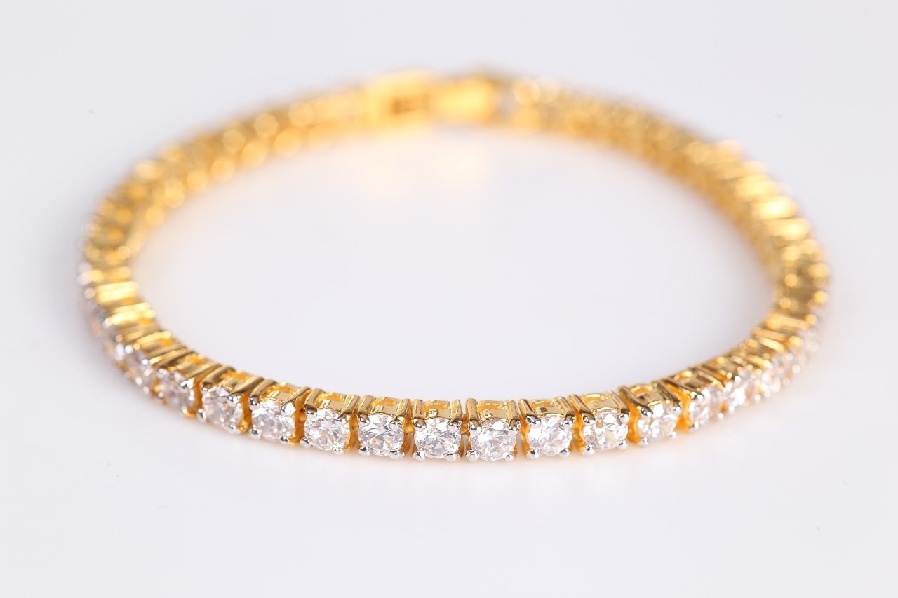 A close-up of a yellow gold and diamond tennis bracelet on a white background.