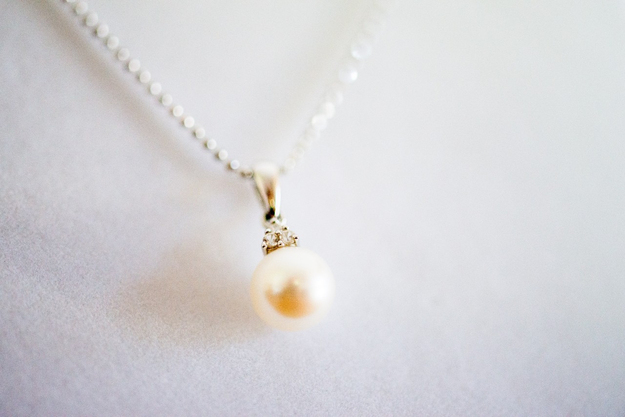 A close-up of a pearl pendant necklace displayed in front of a soft white backdrop.